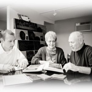Step 1: Choosing the right monument is an important decision. At Weaver Memorials, we will help guide you through the many options and styles available, so you may choose a fitting tribute that fits your needs and budget. Two men and a woman looking at photographs.